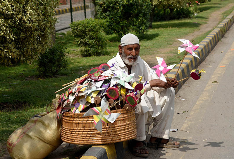 An elderly man is sitting on the footpath selling traditional Toys for Children at Shah Jamal road