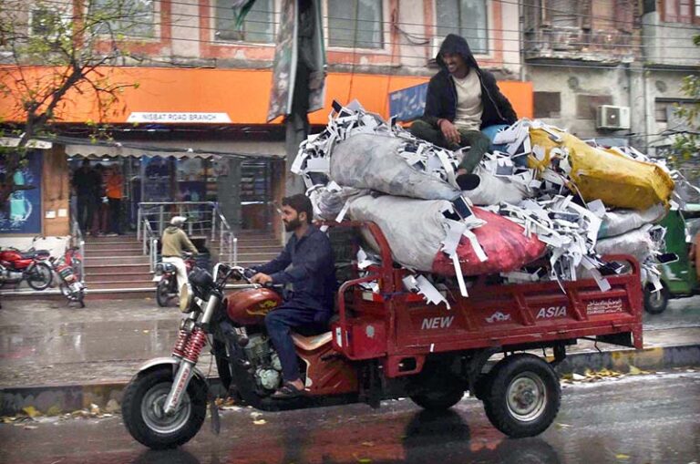A tricycle rickshaw driver on his way loaded with heavy scrap bags at