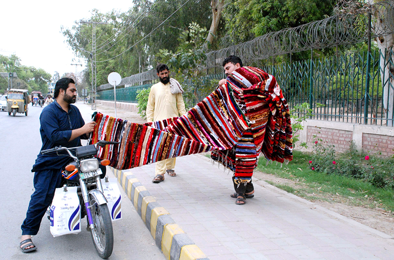 A man is selling handmade carpets of different colors on the roadside