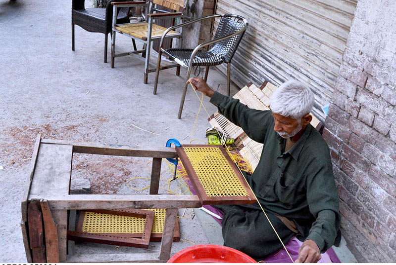 An old man is busy weaving a chair at his workplace near Lahore Hotel Road.