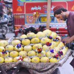 A vendor is decorating melons with flowers and stickers to attract customers