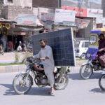 A motorcyclist is carrying a solar panel on the busy City Road