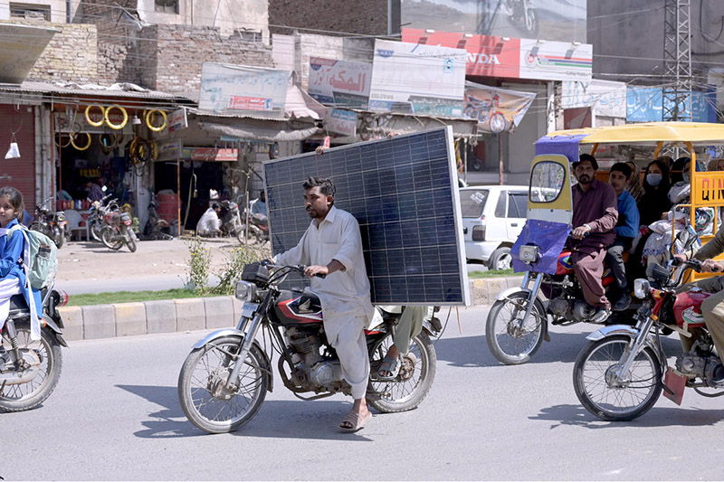 A motorcyclist is carrying a solar panel on the busy City Road