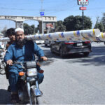 A motorcyclist carrying long plastic pipes on shoulders drives on a busy road puts lives in risk