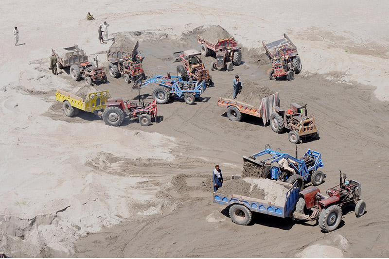 Labourers are busy loading sand on the tractor's trolleys from the dry bed of Chenab River at Head Muhammed Wala