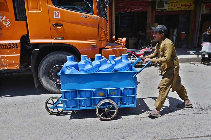 A labourer on the way pushing hand cart loaded with clean drinking water canes to be delivered at shops at Islamabad Fruit and Vegetable Market.