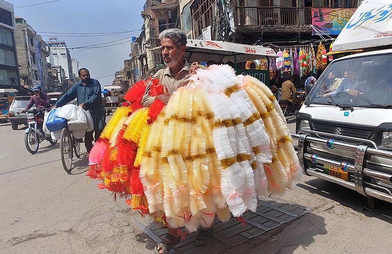 A street vendor on the way carrying different kinds of garlands to attract customers at Ganj Mandi in Raja Bazar.