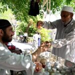 An elderly gentleman selects a fragrance from a vendor's collection at Aabpara Market