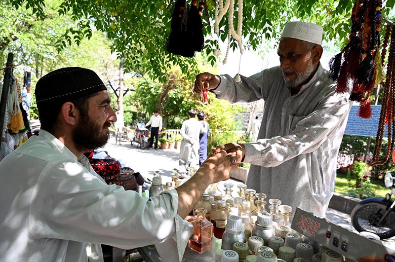 An elderly gentleman selects a fragrance from a vendor's collection at Aabpara Market