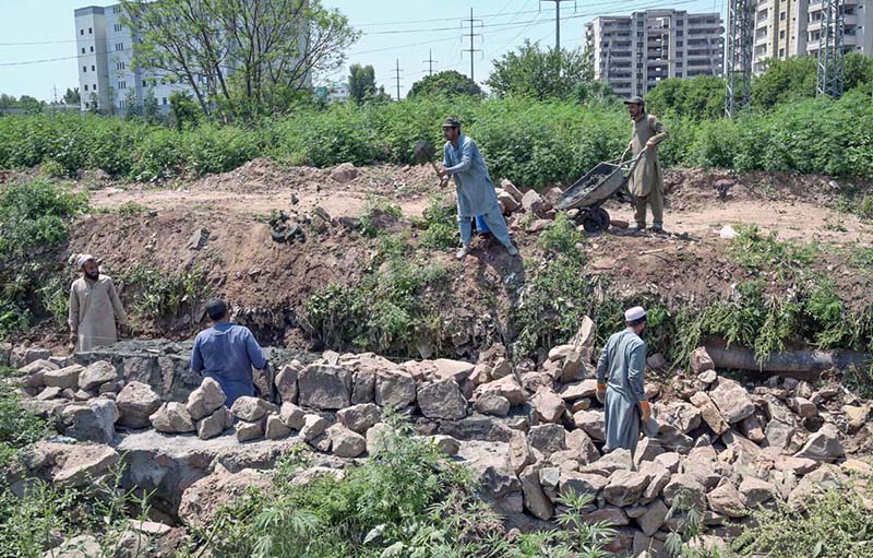 Labourers busy in making wall with stones along road at Tarlahi Chowk in Federal Capital.