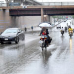 A family traveling on the motorcycle under the cover of umbrellas to protect from rain in the city