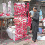 A vendor is preparing flower garlands to attract customers at his roadside setup