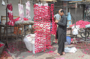 A vendor is preparing flower garlands to attract customers at his roadside setup