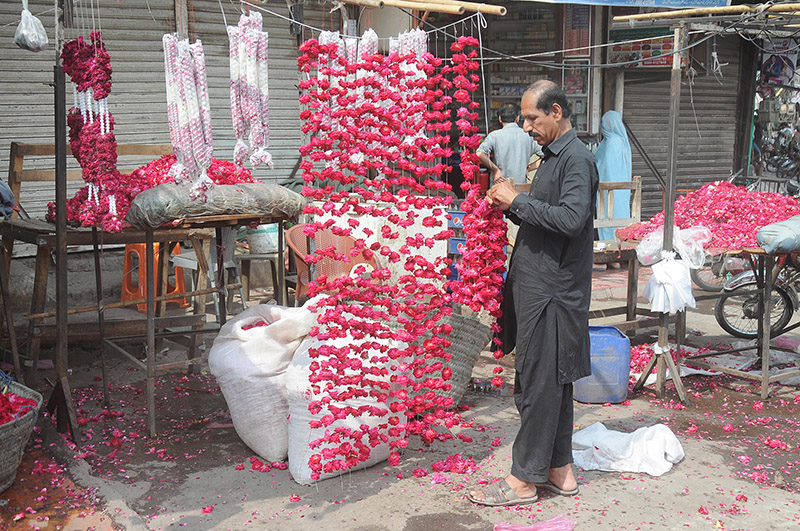 A vendor is preparing flower garlands to attract customers at his roadside setup