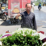 A vendor is busy sprinkling water on the salad to keep them fresh at his hand cart setup