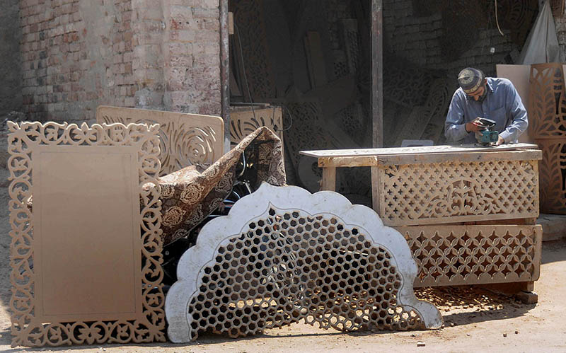 A worker is busy making a design on a wooden sheet with the help of a machine at his workplace