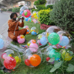A vendor is busy filling the air in the balloons to attract customers at his roadside setup