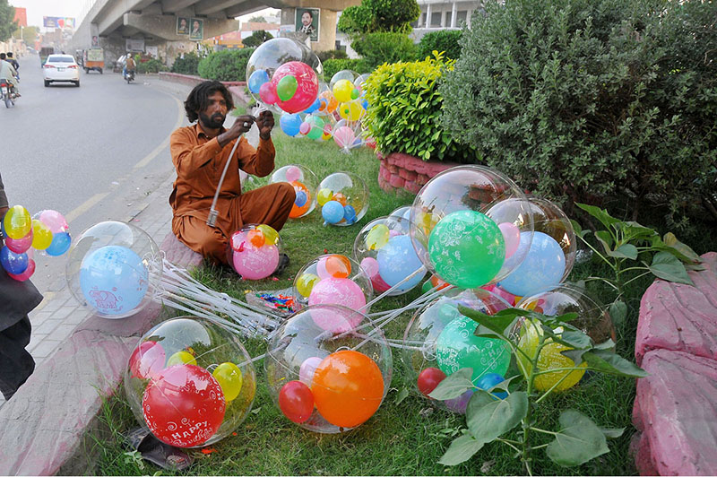 A vendor is busy filling the air in the balloons to attract customers at his roadside setup