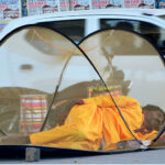 A person seeks nap under a mosquito net on the footpath at Wahdu Wah road