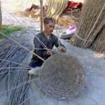 A worker busy in making traditional basket with branches of tree at his workplace
