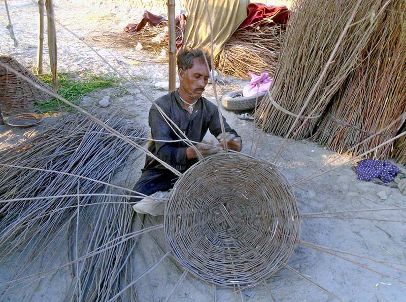 A worker busy in making traditional basket with branches of tree at his workplace