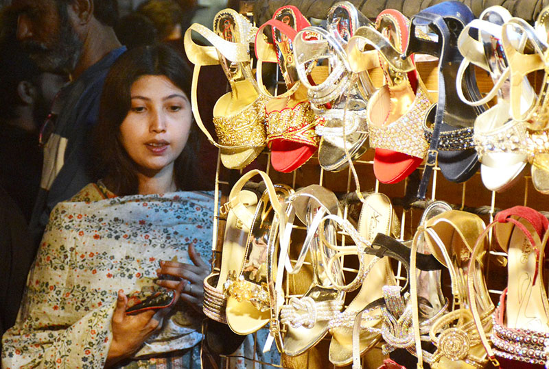 A girl busy in selecting and purchasing sandals from vendor in preparation of upcoming Eid ul fitr at a market