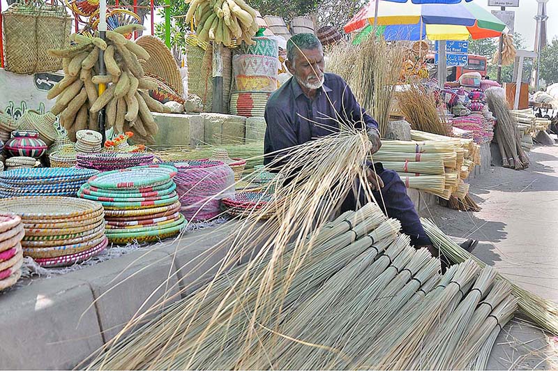 Vendor is busy arranging and displaying traditional brush Brooms and other stuff to attract customers at his roadside setup.
