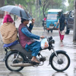 A family traveling on the motorcycle under the cover of umbrella to protect from rain in the city.