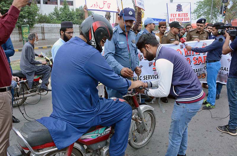 A traffic police personnel installing a kite string protector on a motorcycle for safety measure