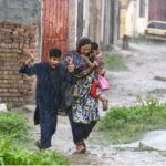 A woman along with children on the way during rain at Tarlahi in the Federal Capital.