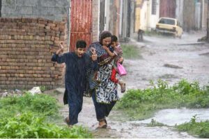 A woman along with children on the way during rain at Tarlahi in the Federal Capital.