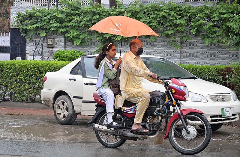 A motorcyclist along with his daughter on the way under the cover of an umbrella to protect from rain that experienced the city.