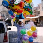 Elderly vendor selling colorful balloons while shuttling on the road