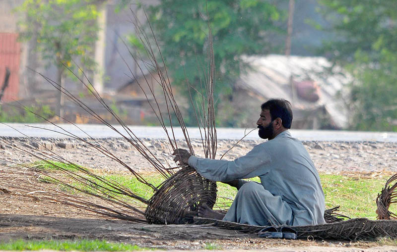 person preparing a basket with dry tree branches to sell for livelihood at his roadside.