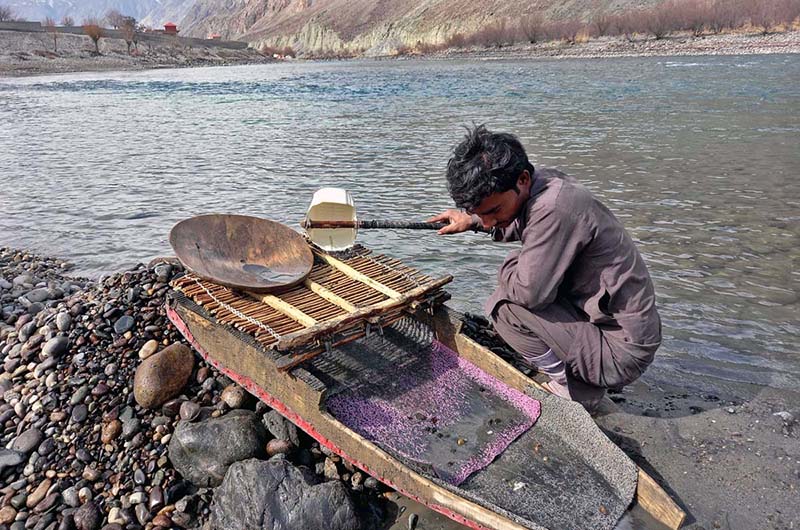 youngster searching for alluvial gold through a traditional way on the bank of river.