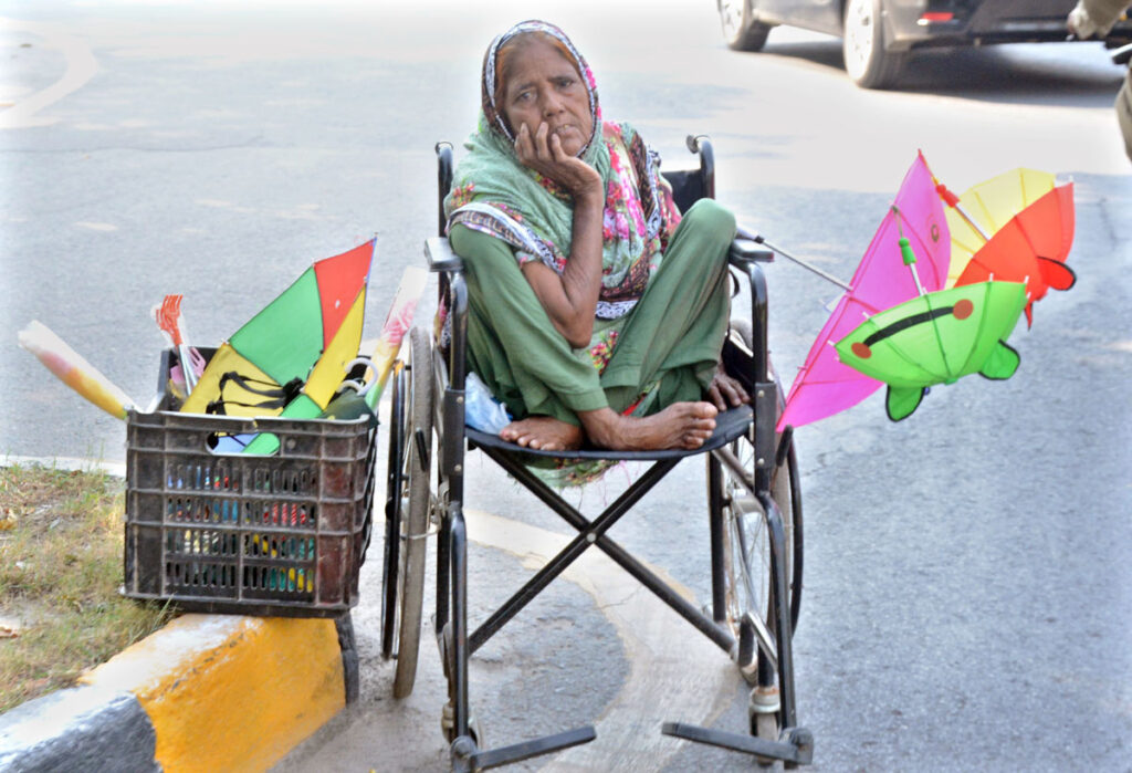 An elderly female vendor selling umbrella for livelihood at roadside.