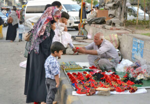 A family purchasing colorful shoes for their children from vendor sitting on footpath along Circular Road.