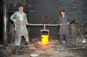 Workers filling melt trash iron into the structure to prepare different new spare parts in the iron molding factory.