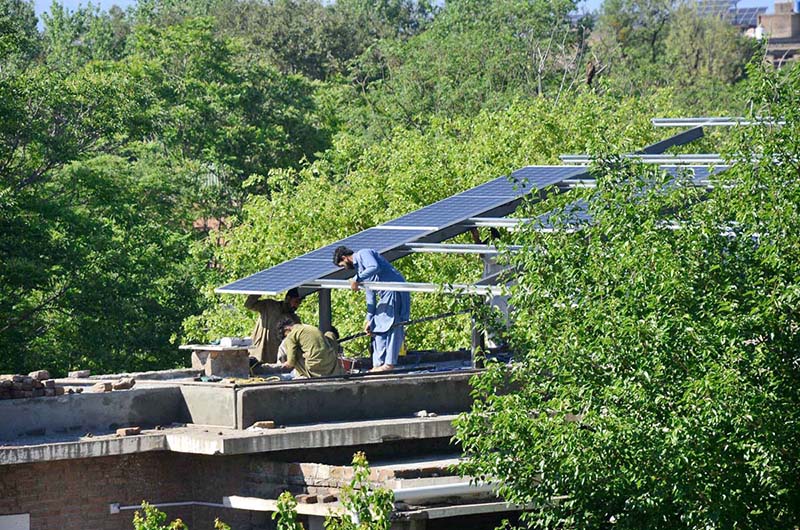 Workers busy in installation of solar panels on the top roof of a house at Bacha Khan Chowk.