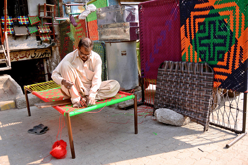 A skilled worker knitting traditional bed (Charpoi) at his workplace in the city