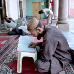 A person is engrossed in reciting the Holy Quran in Jamia Masjid Noori
