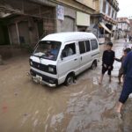 A vehicle and people passing through rain water in street after heavy rain at Charsadda Road