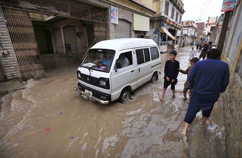 A vehicle and people passing through rain water in street after heavy rain at Charsadda Road