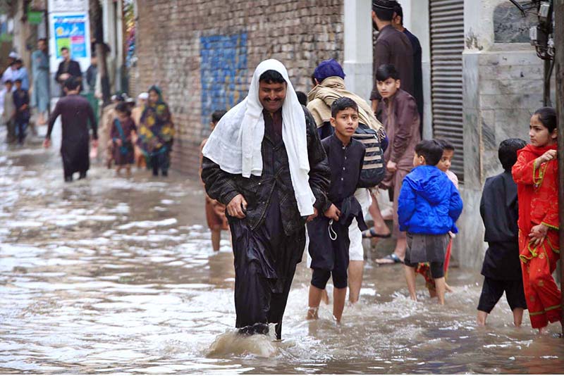 A vehicle and people passing through rain water in street after heavy rain at Charsadda Road