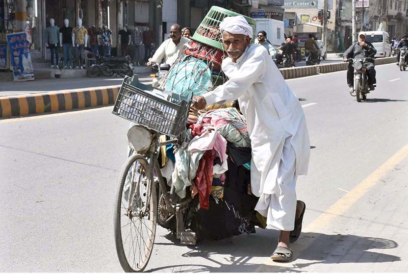 An aged man on his way pushing his bicycle loaded with domestic use items to sell for livelihood.