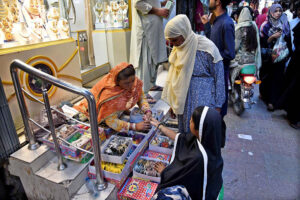 A vendor to put on bangles to a girl at Resham Gali during Eid shopping