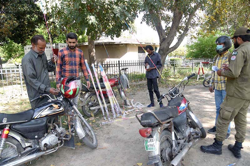 In order to protect the motorcyclist from a dangerous accident due to the use of metal strings used in Kiting, a man is fixing a plastic rod on the motorcycle while a policeman witnessing it.