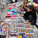 A vendor to put on bangles to a girl at Resham Gali during Eid shopping