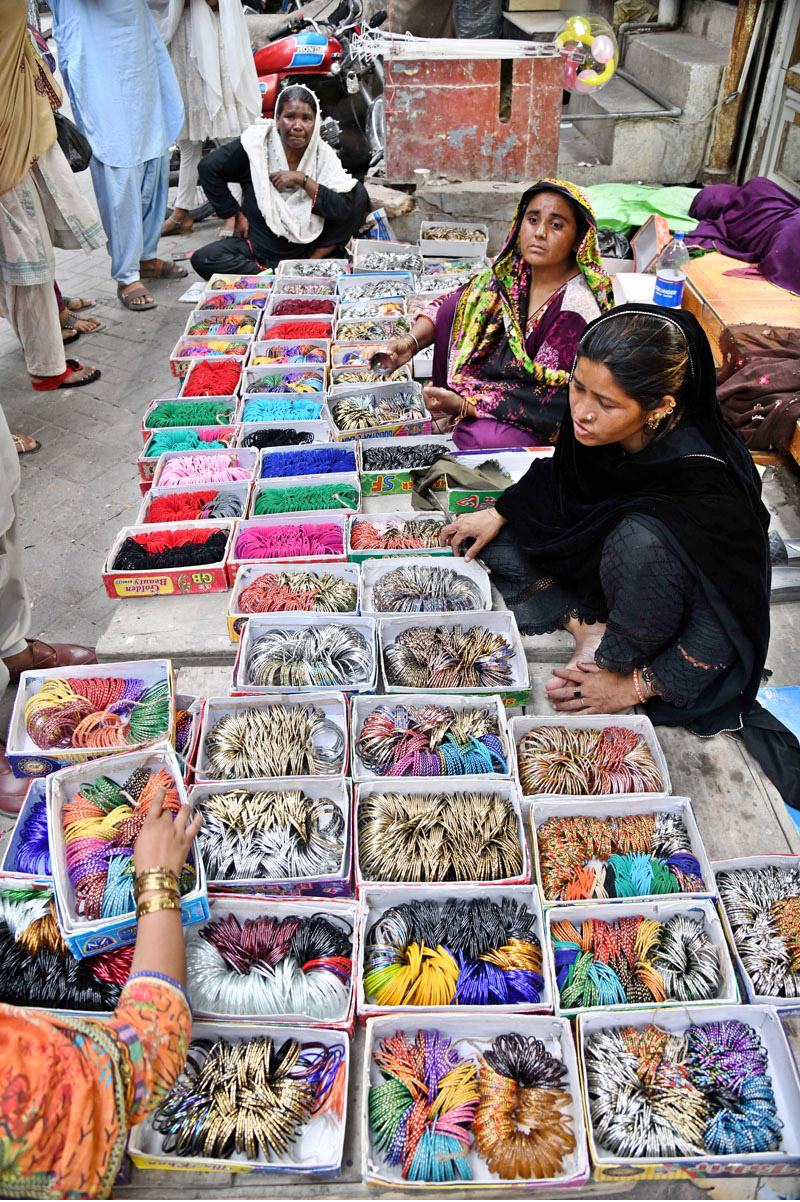 A vendor to put on bangles to a girl at Resham Gali during Eid shopping