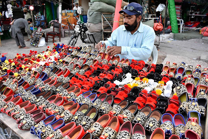vendor arranging and displaying the colorful handmade children shoes to attract the customers on his handcart outside the Naulakha Bazaar.